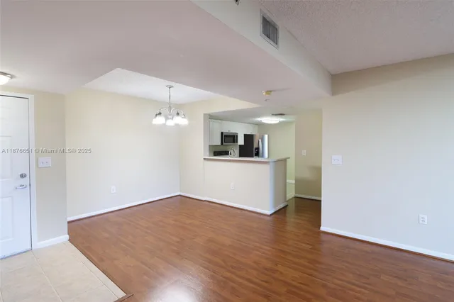 an empty room with wooden floor and kitchen view