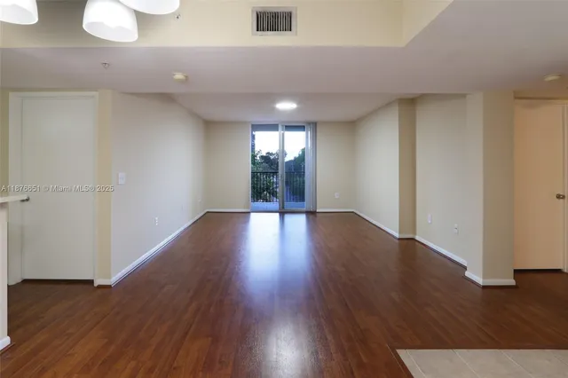 a view of an empty room with wooden floor and window