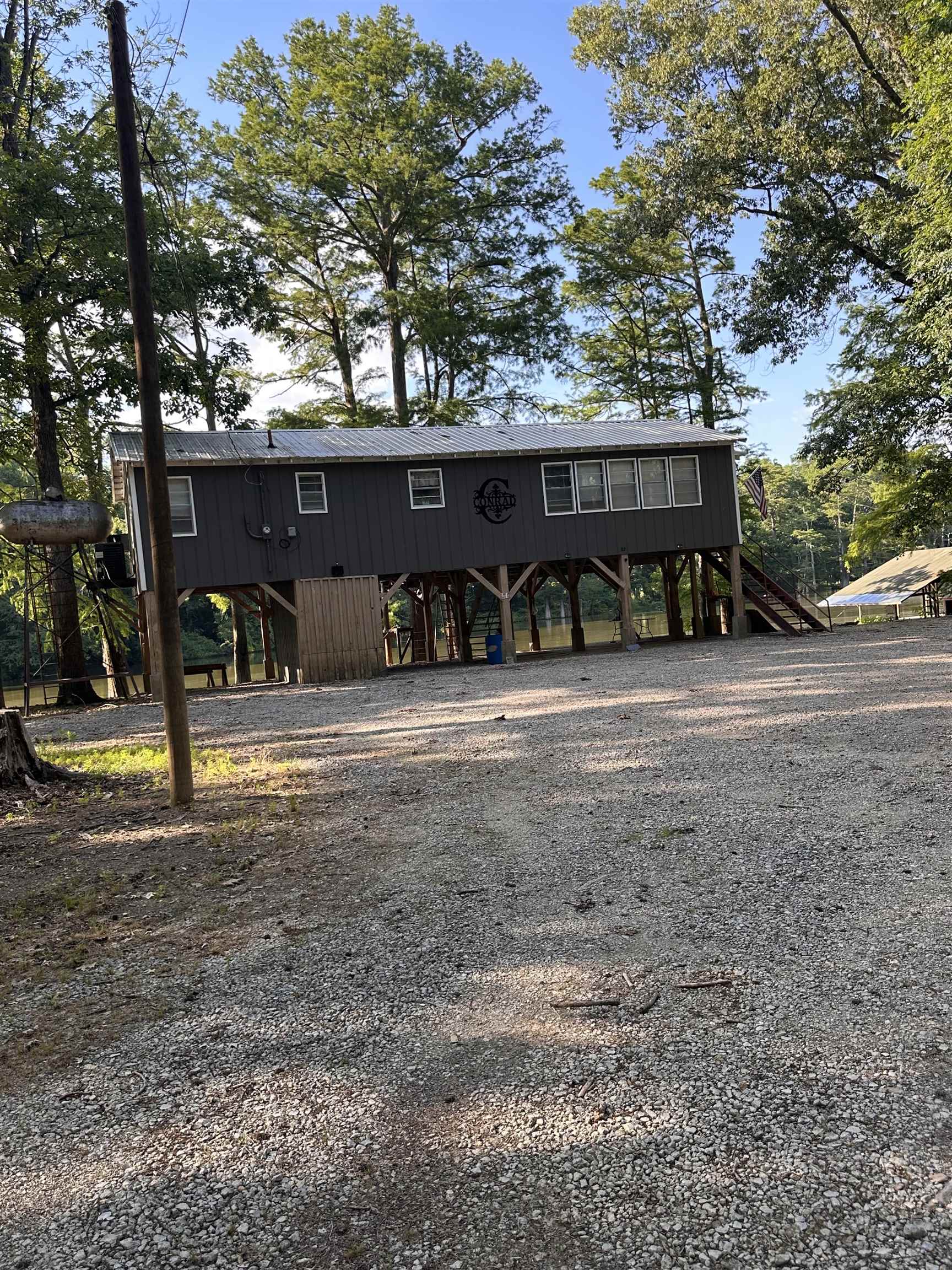 481 Chisholm Lake Camp Road Ripley, TN 38063 - Photo 1 of 12 Raised structure featuring a dark siding facade, multiple windows, a metal roof, and a gravel parking area
