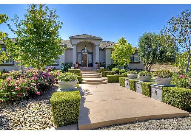 Grand entrance framed by a lushly landscaped walkway at the end of crushed stone driveway