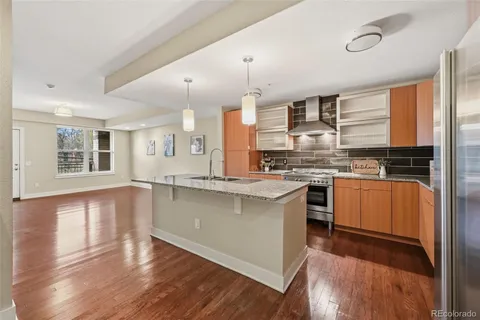 a kitchen with stainless steel appliances kitchen island granite countertop a stove a sink a refrigerator and white cabinets with wooden floor