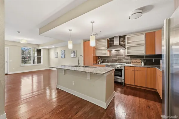 a kitchen with stainless steel appliances kitchen island granite countertop a stove a sink a refrigerator and white cabinets with wooden floor