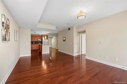 a view of empty room with wooden floor and kitchen view