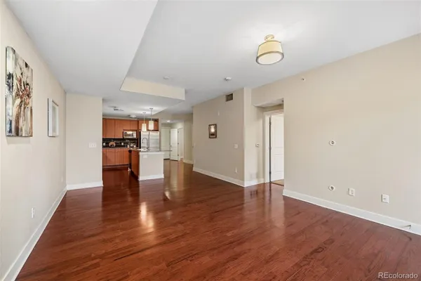 a view of empty room with wooden floor and kitchen view