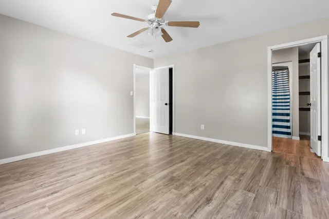 a view of an empty room with wooden floor and a ceiling fan