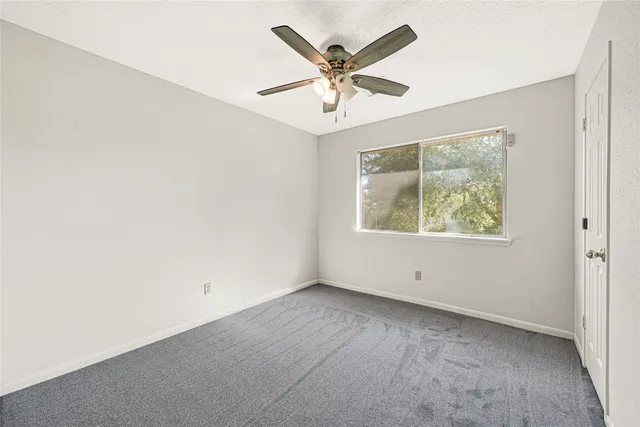 an empty room with wooden floor chandelier fan and windows