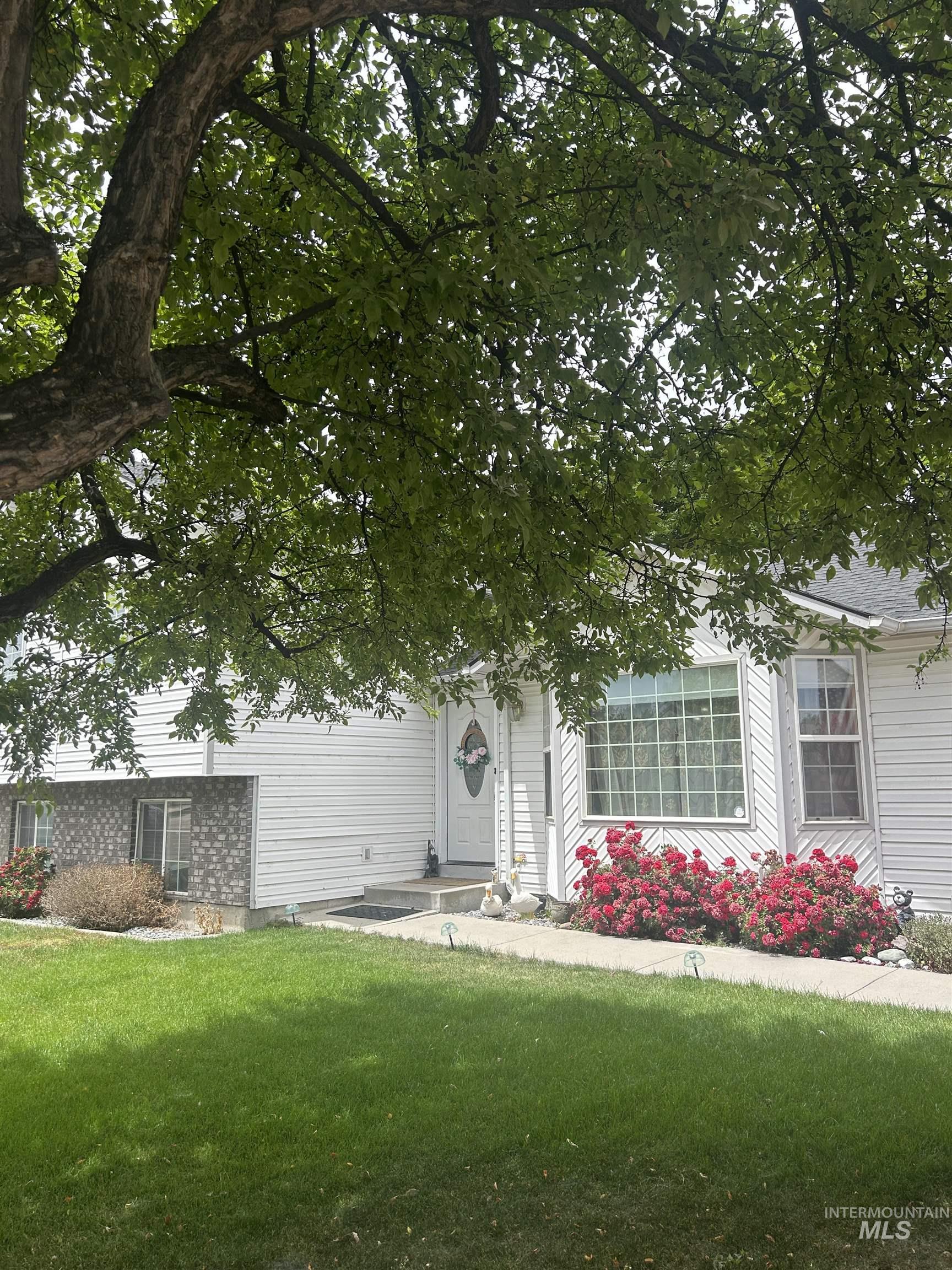 1444 East Doberman Street Meridian, ID 83642 - Photo 3 of 31 White siding exterior with a stone accent facade, featuring a front entry with a decorative door, a multi-pane window, landscaped shrubbery, and a mature tree providing natural shade