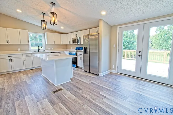 a kitchen with stainless steel appliances granite countertop a stove a refrigerator a sink and white cabinets with wooden floor next to windows