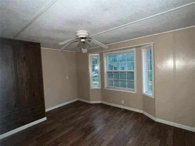 an empty room with wooden floor fan and windows