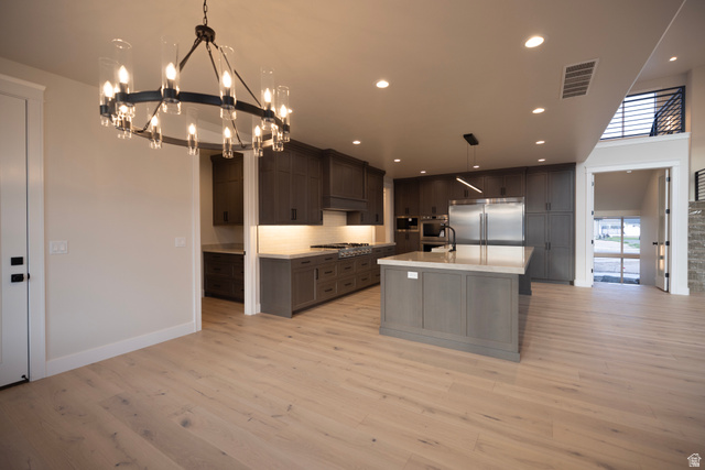 904 South 1900 West Layton, UT 84041 - Photo 9 of 19 Kitchen featuring stainless steel appliances, an island with sink, light wood finished floors, suspended lighting, and decorative backsplash