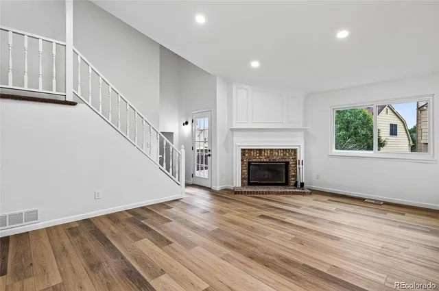 a view of an empty room with wooden floor fireplace and a window