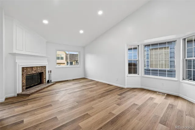 a view of an empty room with wooden floor fireplace and a window
