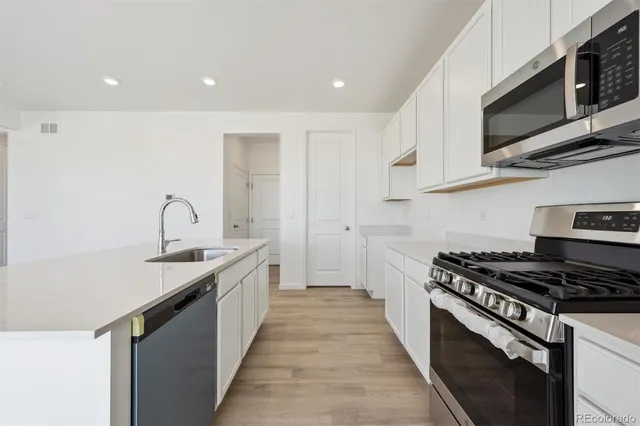 a kitchen with stainless steel appliances a sink dishwasher stove top oven and cabinets with wooden floor