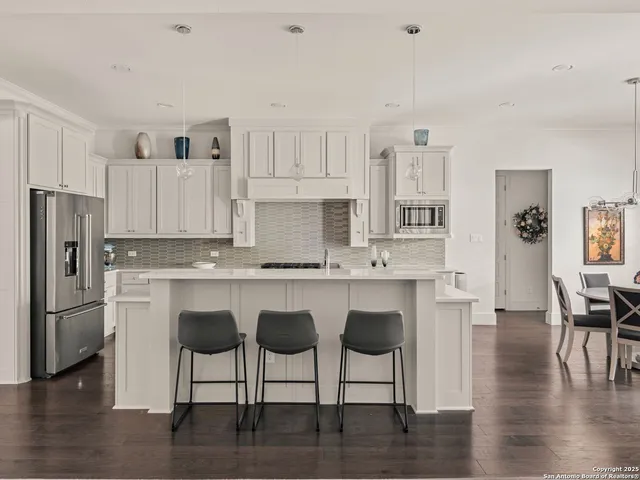 a kitchen with stainless steel appliances granite countertop a stove top oven a refrigerator a sink and a dining table with wooden floor