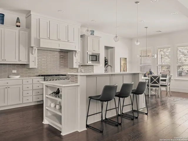 a kitchen with stainless steel appliances granite countertop a stove top oven a sink a dining table and chairs with wooden floor