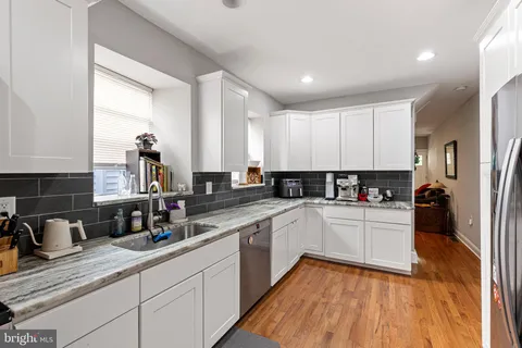 a kitchen with a sink dishwasher a refrigerator and white cabinets with wooden floor
