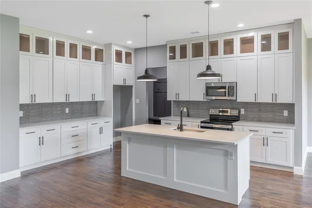 a kitchen with stainless steel appliances granite countertop a stove a sink dishwasher a refrigerator and white cabinets with wooden floor