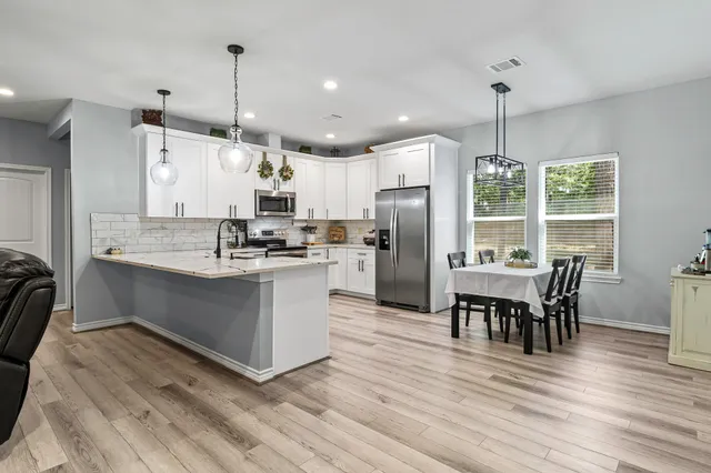 a kitchen with stainless steel appliances kitchen island granite countertop a refrigerator a stove a dining table and chairs with wooden floor