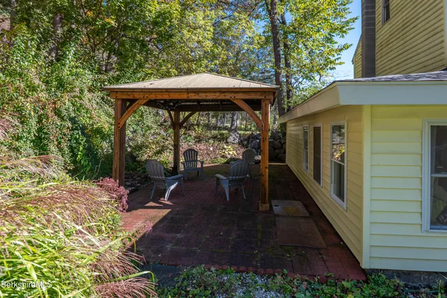 a view of a patio with table and chairs under an umbrella with large trees