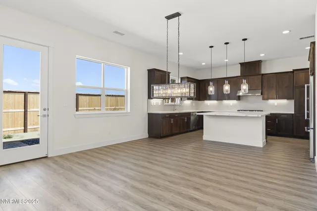 a large kitchen with stainless steel appliances granite countertop a stove a sink dishwasher a refrigerator and white cabinets with wooden floor