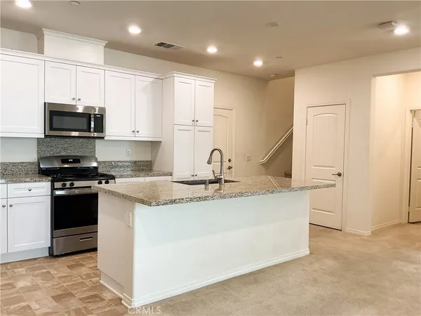 a kitchen with stainless steel appliances granite countertop a sink a stove and a refrigerator with white cabinets