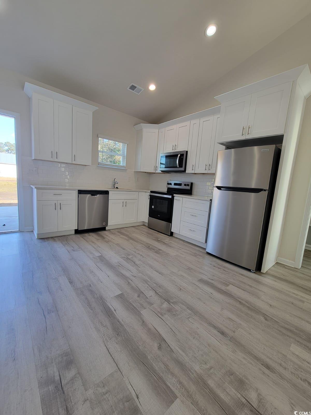 4967 Lyons Lane Longs, SC 29568 - Photo 6 of 9 Kitchen featuring tasteful backsplash, white cabinetry, stainless steel appliances, vaulted ceiling, and light wood-style floors