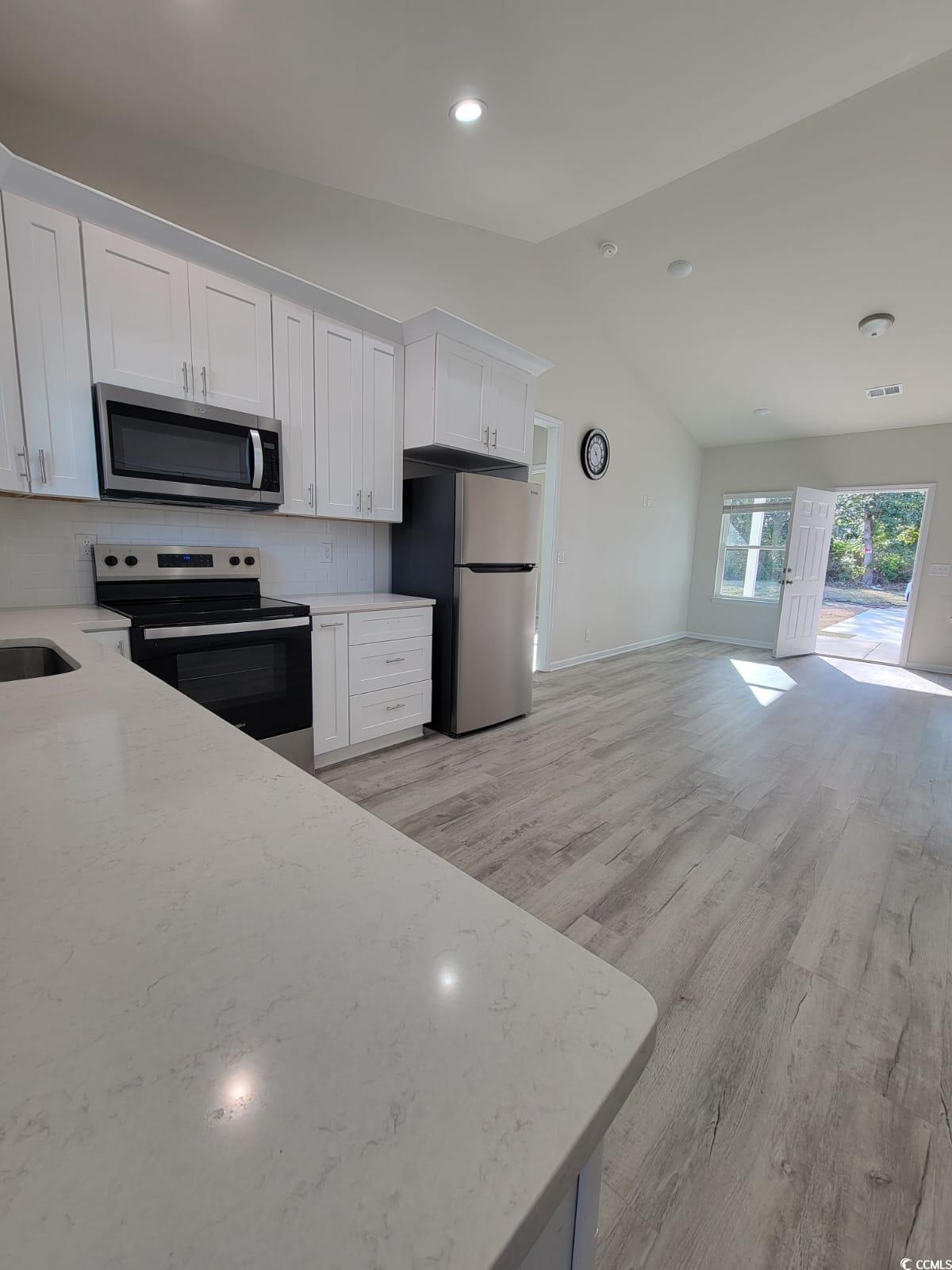 4967 Lyons Lane Longs, SC 29568 - Photo 9 of 9 Kitchen with appliances with stainless steel finishes, white cabinetry, vaulted ceiling, tasteful backsplash, and light stone countertops