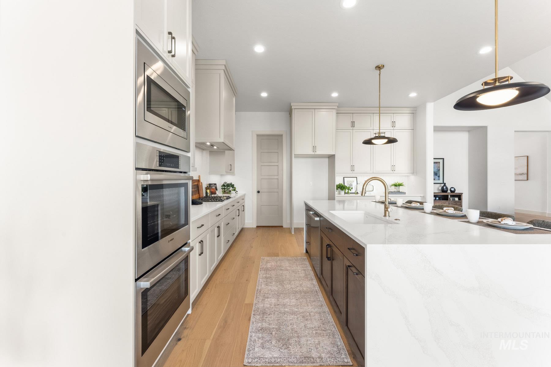 6954 Saddle Bred Way Star, ID 83669 - Photo 12 of 50 Two tone kitchen with two tone cabinets, light stone countertops, stainless steel appliances, light wood-type flooring, and pendant lighting