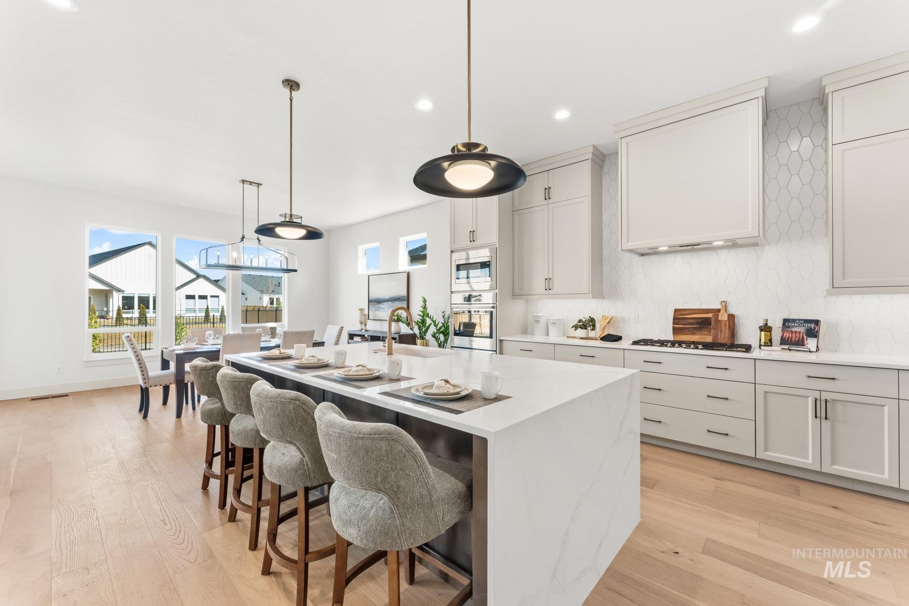 6954 Saddle Bred Way Star, ID 83669 - Photo 15 of 50 Kitchen featuring decorative backsplash, stainless steel appliances, light wood finished floors, pendant lighting, and light stone countertops