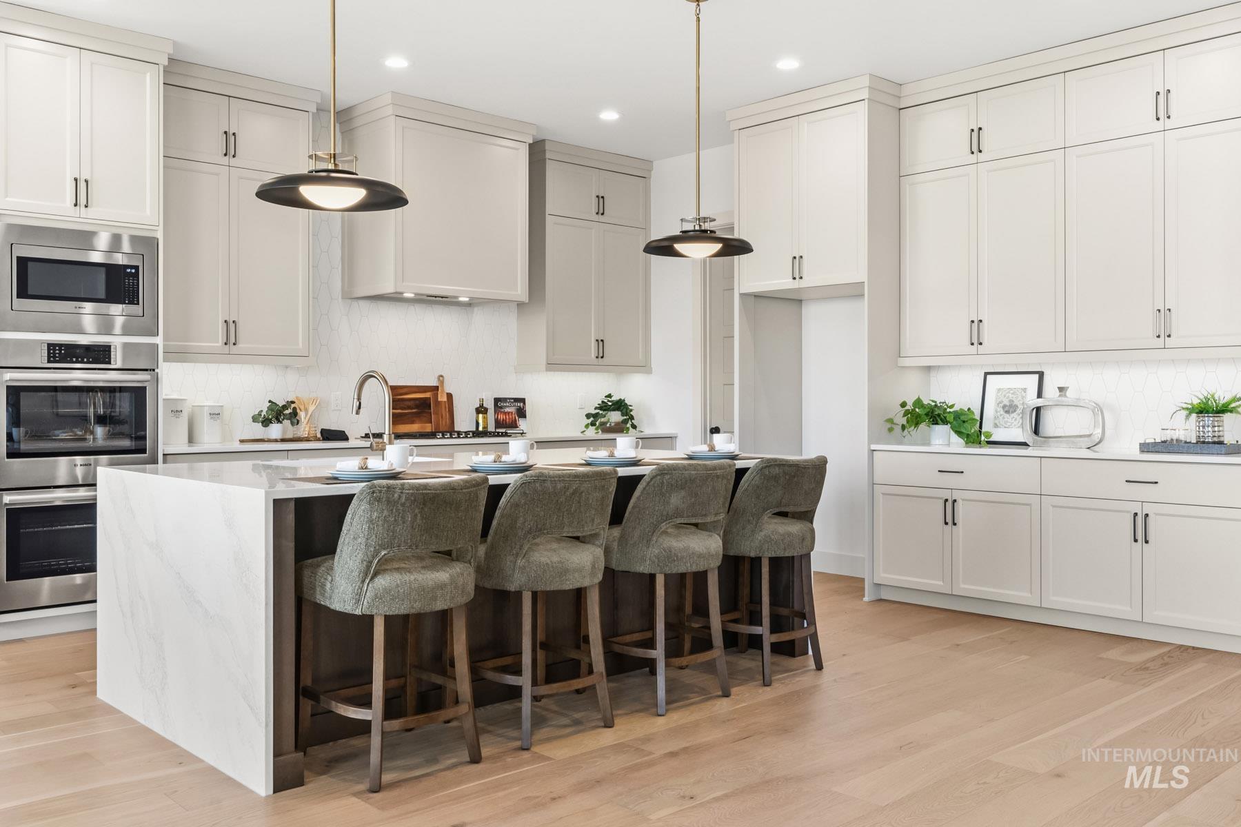 6954 Saddle Bred Way Star, ID 83669 - Photo 5 of 50 Two tone kitchen with light stone counters, stainless steel appliances, tasteful backsplash, light wood finished floors, and an island with sink