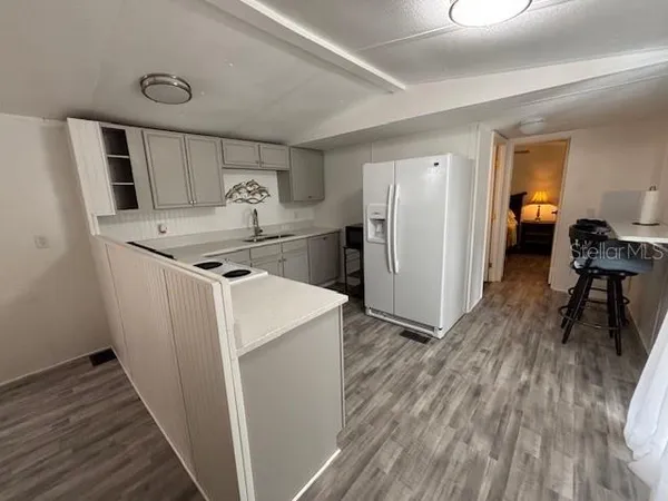 a view of a refrigerator in kitchen and an empty room with wooden floor