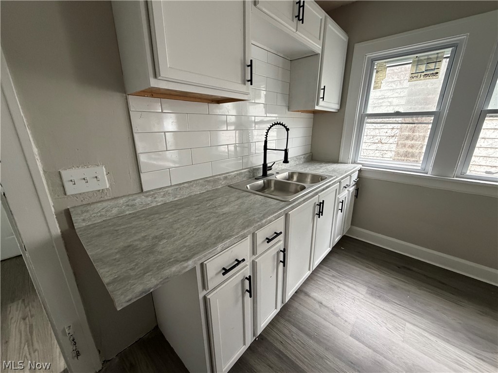 15317 Shiloh Road Cleveland, OH 44110 - Photo 12 of 29 Kitchen featuring white shaker-style cabinetry with matte black hardware, dual-basin stainless steel sink with a matte black faucet, subway tile backsplash, and light-toned, wood-finish flooring