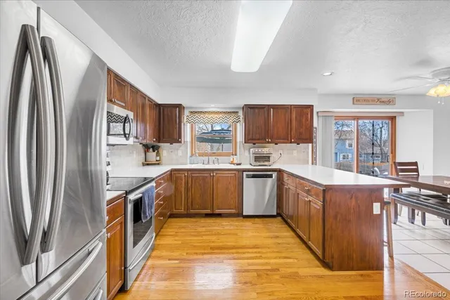 a large kitchen with stainless steel appliances granite countertop a stove a sink dishwasher a refrigerator and a dining table with wooden floor