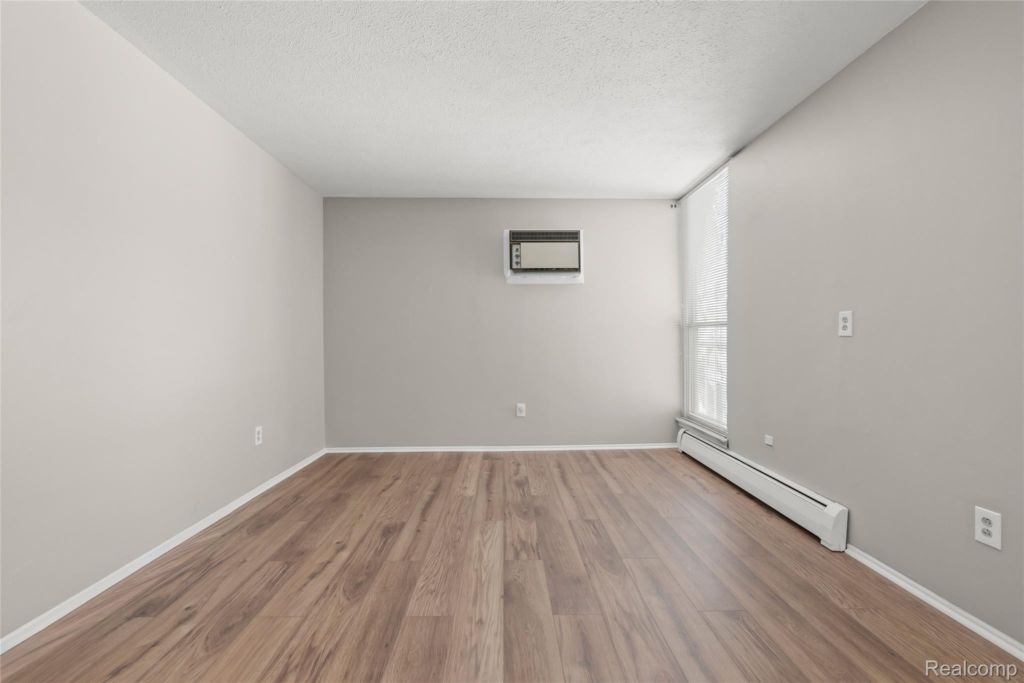4909 Crooks Road, Unit D6 Royal Oak, MI 48073 - Photo 12 of 16 Unfurnished Primary bedroom featuring a baseboard radiator, new wood laminate floors, a textured ceiling, and a wall unit AC