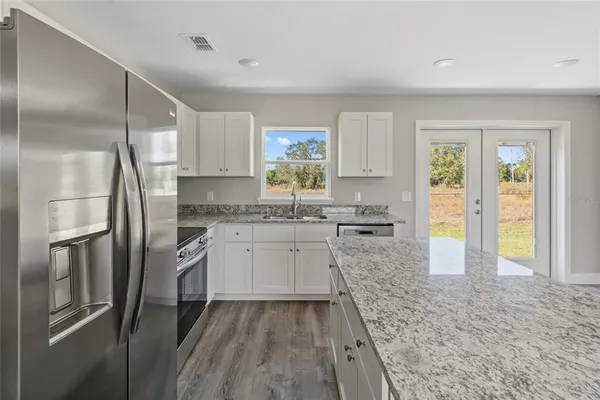 a kitchen with stainless steel appliances granite countertop a refrigerator a stove and a sink with large window