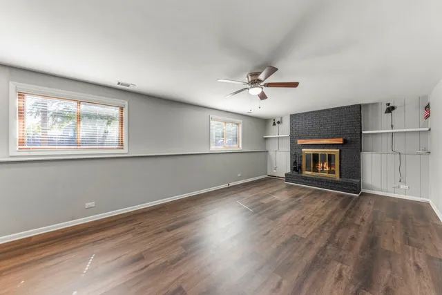 an empty room with wooden floor fireplace and windows