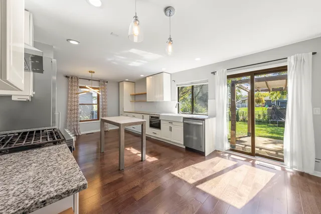 a open kitchen with granite countertop a stove a sink a dining table and chairs with wooden floor