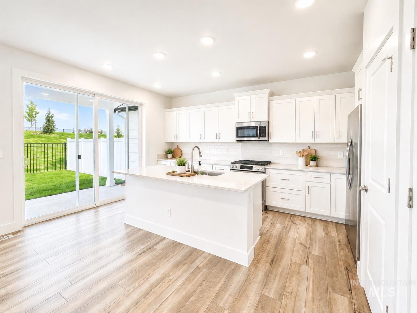 8098 West Fern Street Eagle, ID 83616 - Photo 4 of 22 Modern kitchen featuring white shaker cabinetry, stainless steel appliances, a center island with sink, and wood-finish flooring