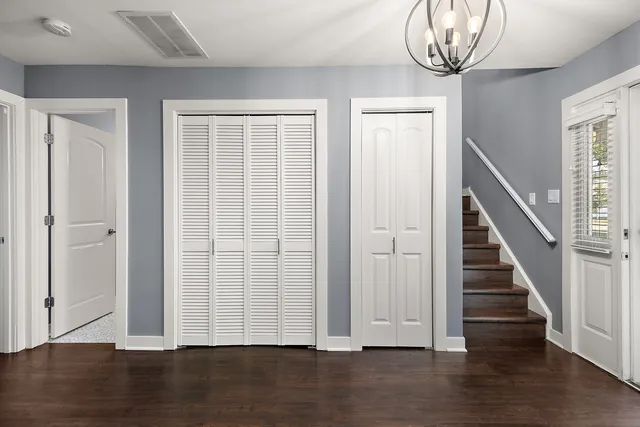 an empty room with wooden floor staircase and windows