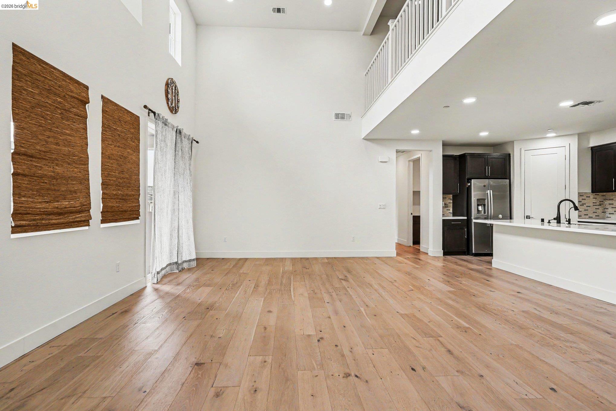 18210 Argento Loop San Ramon, CA 94583 - Photo 8 of 44 Open-concept living area featuring high ceilings, wood-finish flooring, and a kitchen with dark cabinetry, stainless steel appliances, and a tiled backsplash