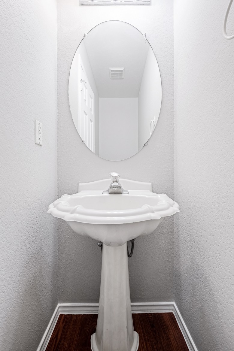 3709 Crownover Street Austin, TX 78725 - Photo 14 of 26 This powder room features a classic white pedestal sink, an oval wall-mounted mirror, and dark wood-look flooring