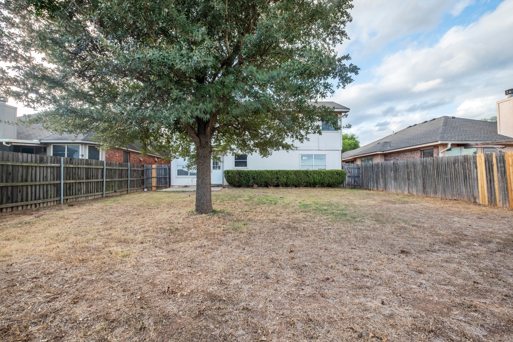3709 Crownover Street Austin, TX 78725 - Photo 25 of 26 The property features a spacious backyard with a mature tree, a wooden privacy fence, and a well-maintained shrub border