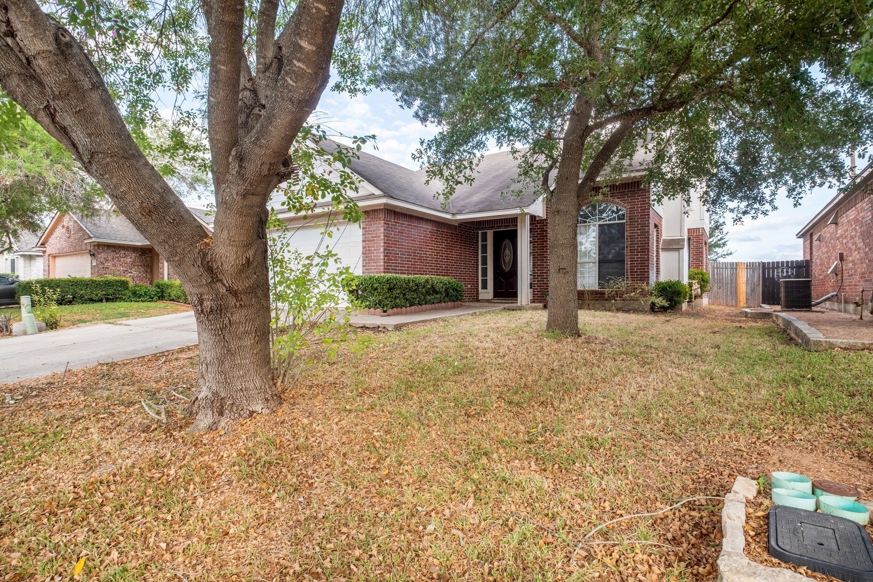 3709 Crownover Street Austin, TX 78725 - Photo 3 of 26 The property features a brick exterior with white trim, a front yard with mature trees, and a paved driveway leading to an attached garage