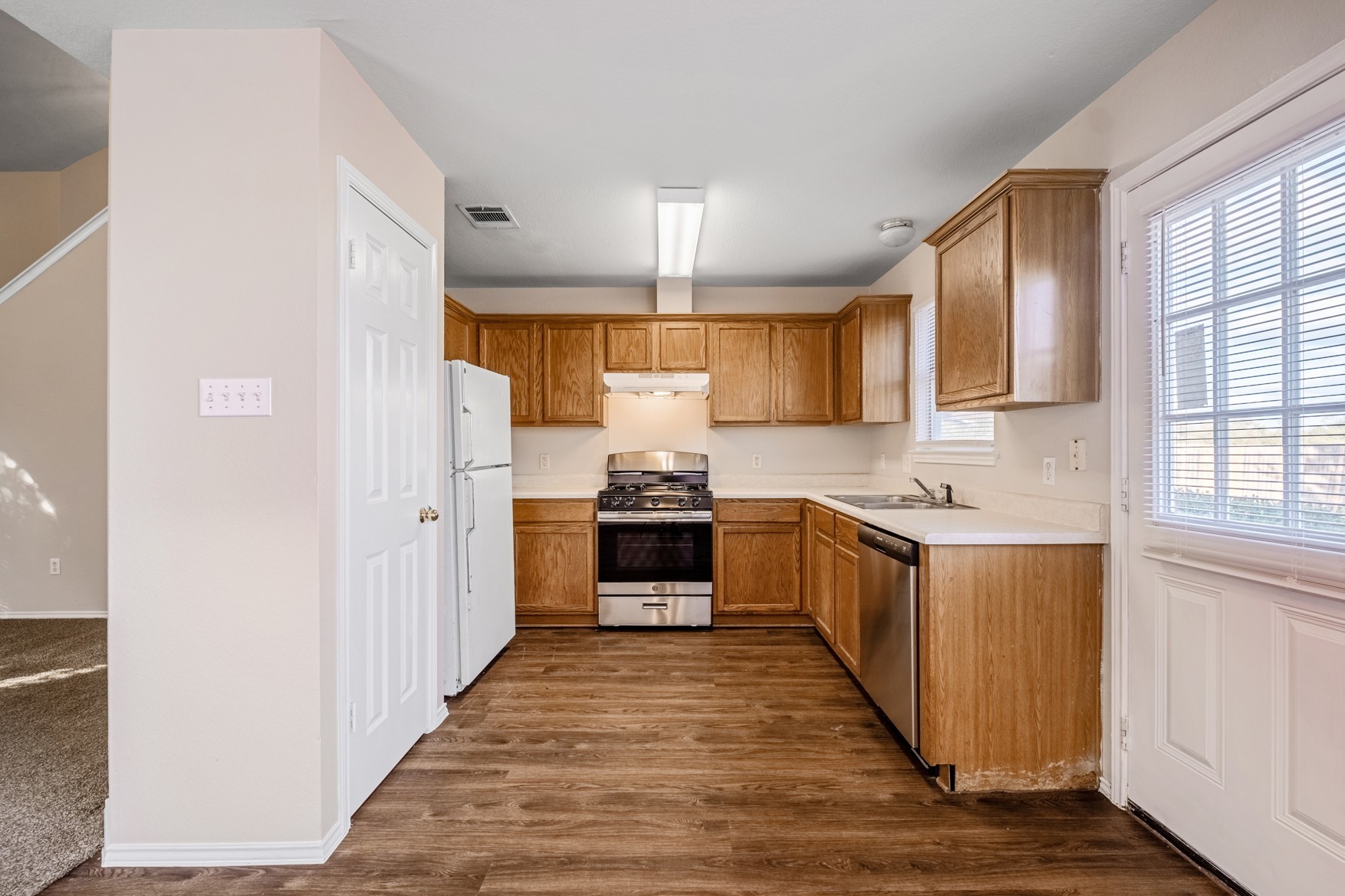 3709 Crownover Street Austin, TX 78725 - Photo 8 of 26 The kitchen features wood-look flooring, light wood cabinetry, a stainless steel oven/range, a white refrigerator, and a window with blinds