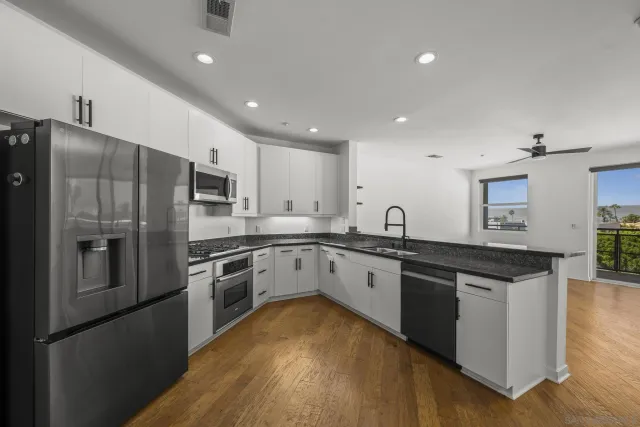 a large kitchen with stainless steel appliances granite countertop a stove a sink dishwasher a refrigerator and white cabinets with wooden floor
