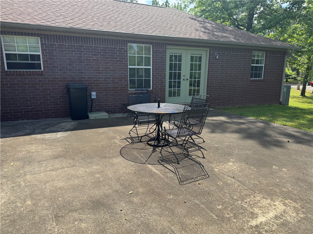 95 Deer Run Road Delaware, AR 72835 - Photo 38 of 40 Concrete patio area with a brick exterior, featuring light green double French doors, multiple windows with white frames, and a shingled roof