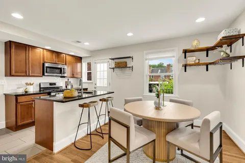 a kitchen with stainless steel appliances granite countertop a stove a sink a refrigerator a microwave a dining table and chairs with wooden floor