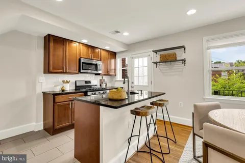 a kitchen with stainless steel appliances granite countertop a stove top oven a sink dishwasher a dining table and chairs with wooden floor
