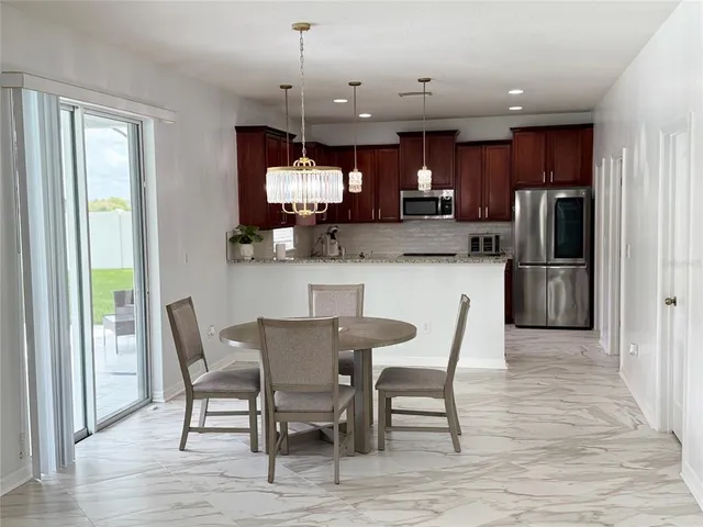 a kitchen with stainless steel appliances granite countertop a dining table chairs refrigerator and microwave