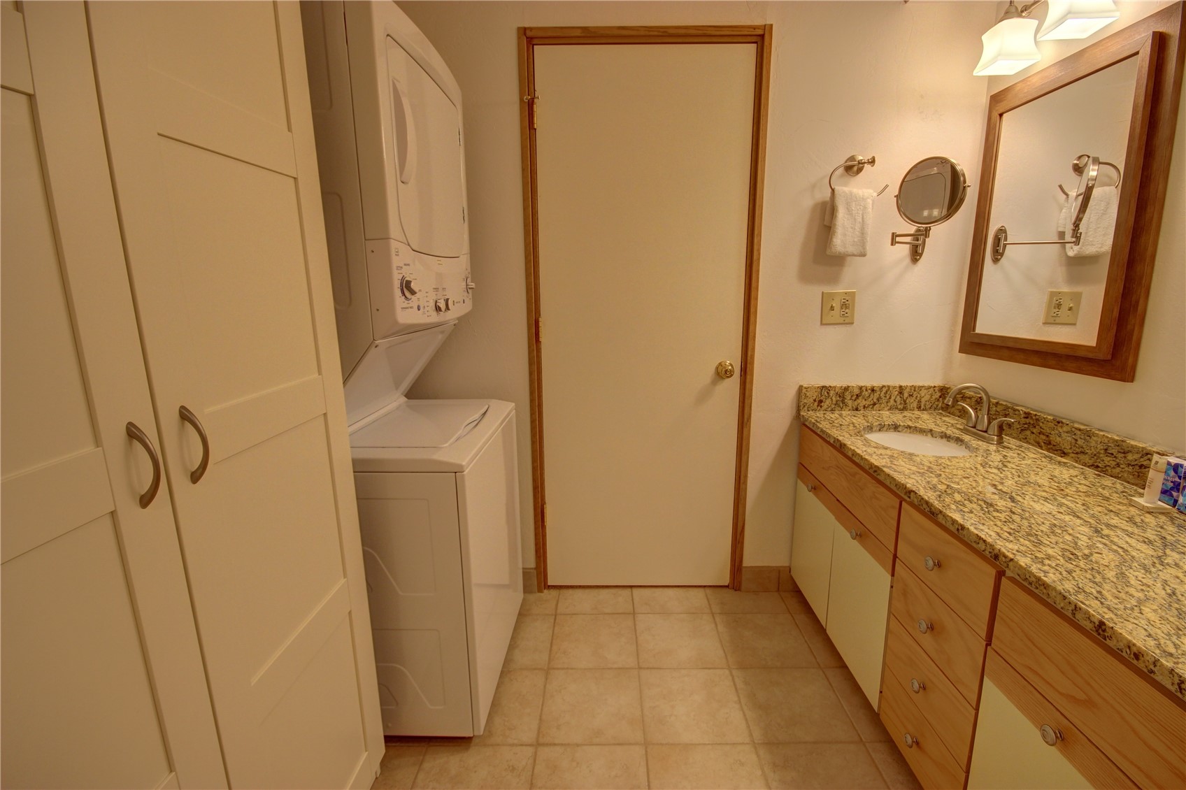 Washroom with light tile patterned floors, stacked washer / dryer, and sink